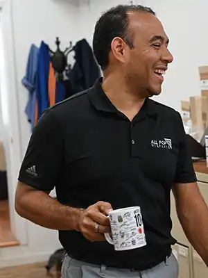 Gerardo Araujo smiling with his cup of coffee in his right hand dressed in his blue All POP Displays t-shirt